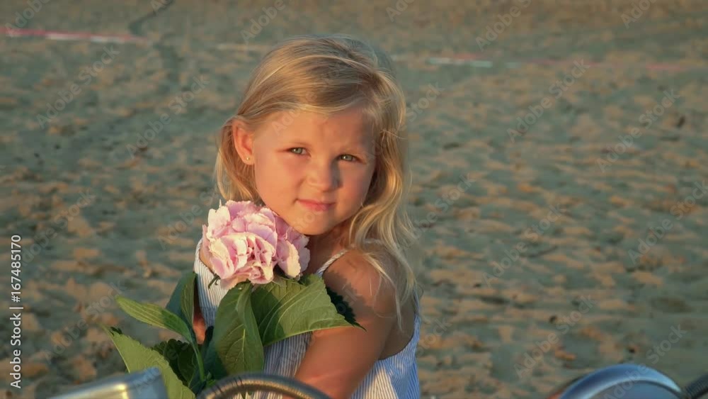 The beautiful girl the blonde looks in the camera sitting on the seashore The beautiful girl the blonde looks in the camera sitting on the seashore