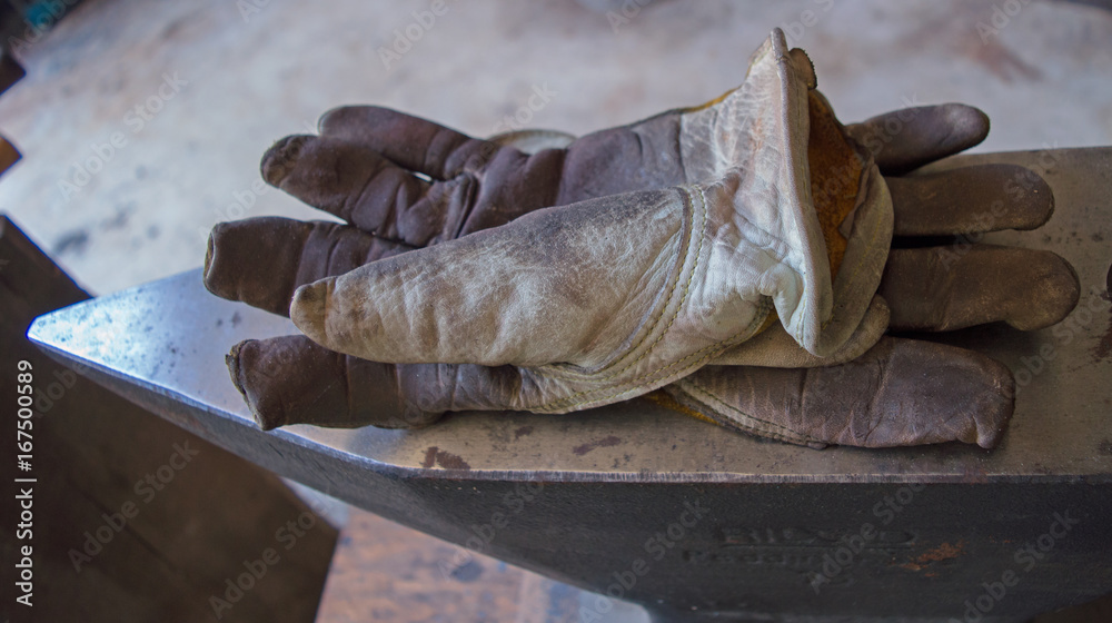 Moving on to other chores, the blacksmith leaves his well used gloves on top of the metal anvil inside the workshop.