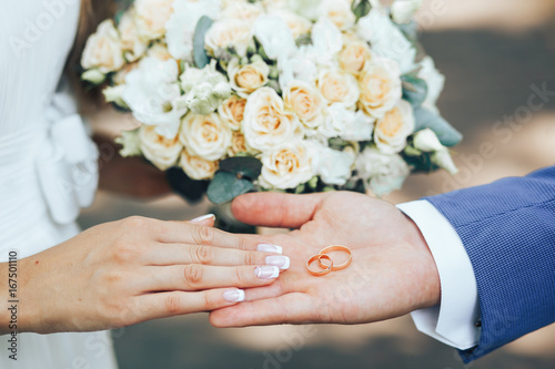 the groom on the hand holds two gold wedding rings bride lends a helping hand to the rings