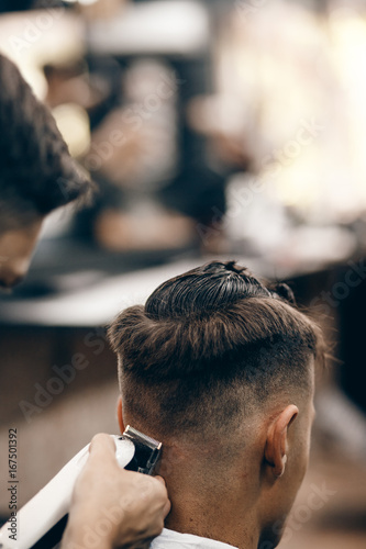 Male hippy customer in barber shop hairdresser on fashionable haircut, rear view. They cut her hair, put her hair dryer and wax. Concept of hair care. Toned photo.