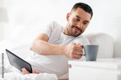 man with tablet pc drinking coffee in bed at home