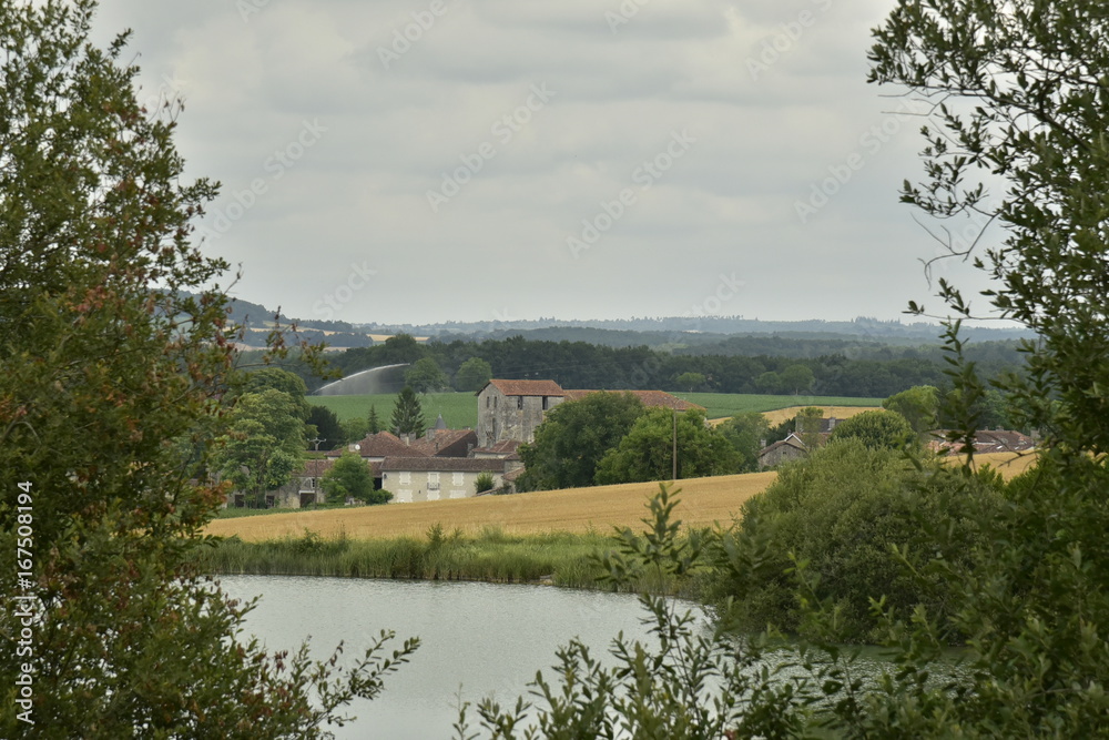 Derrière l'étang aux eaux couleur émeraude ,le village de Champagne avec son église romane ,au Périgord Vert 