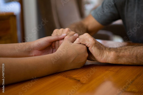 Female doctor and senior man holding hands at table