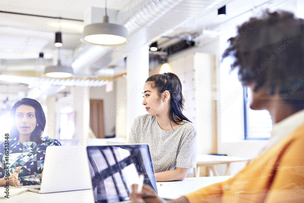 Businesswomen looking at female colleague explaining while sitting at conference table Businesswomen looking at female colleague explaining while sitting at conference table