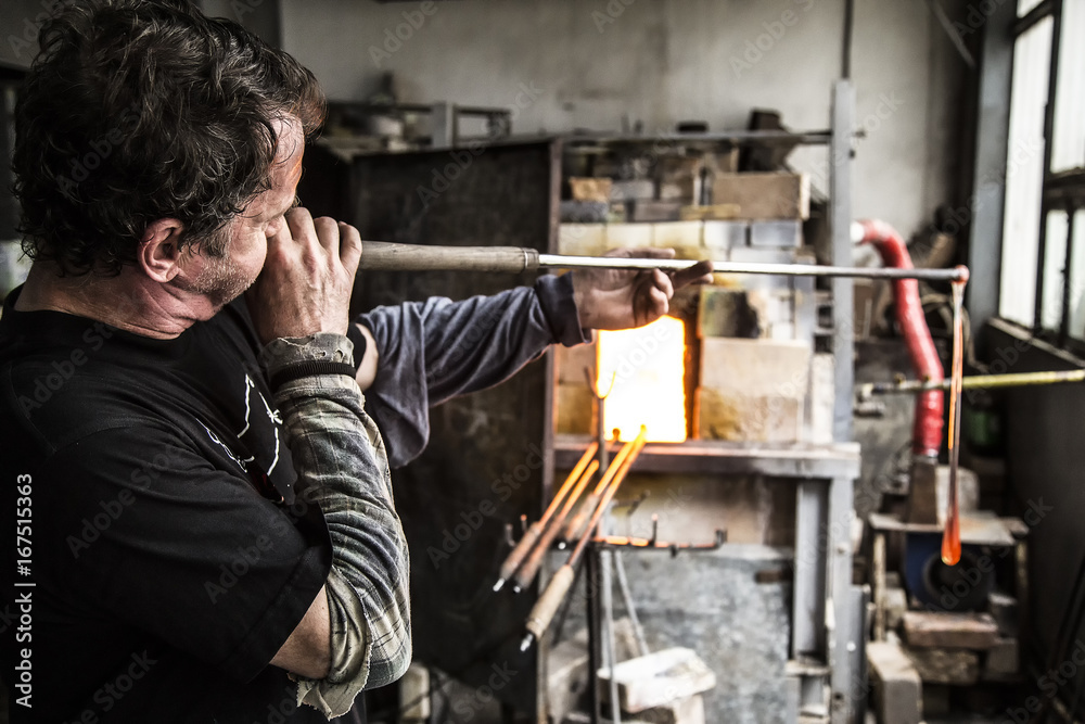 Side view of glass blower blowing molten glass with tube in factory Side view of glass blower blowing molten glass with tube in factory