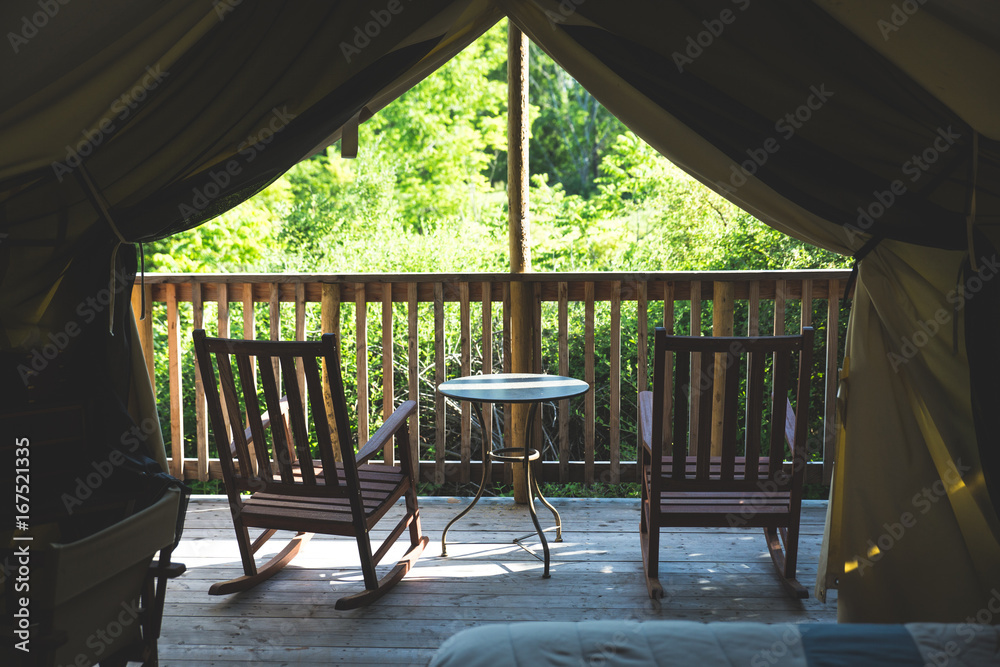 Interior of tent cabin in the woods with two chairs and table on deck