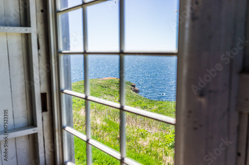 Looking through old window of house with cliff and ocean view in Bonaventure Island  Quebec  Canada