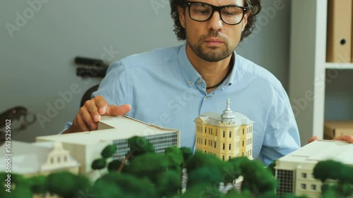 Young architect looking to the camera, crossing hands and smiling in the modern office with city model. photo