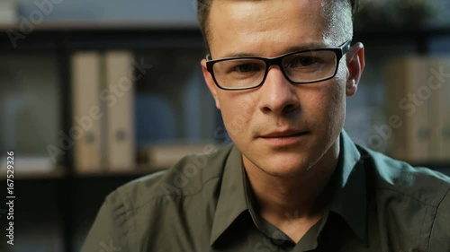 Portrait of attractive young business man in the stylish glasses looking to the camera in the modern office background.