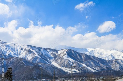 Hakuba mountain range in the winter with snow on the mountain and blue sky and clouds background in Hakuba Nagano Japan.