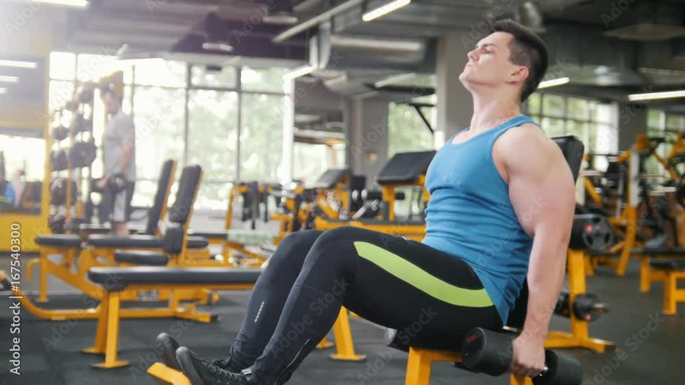 Bodybuilding in the gym - young sporty man performs training for arm with dumbbells