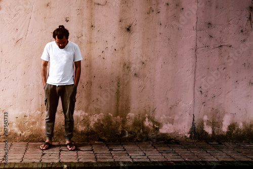Asian man stands bend down the head by have a old walls is in behind.