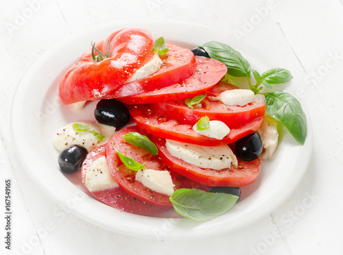 Foto Tomato and mozzarella slices with basil leaves on a white plate.