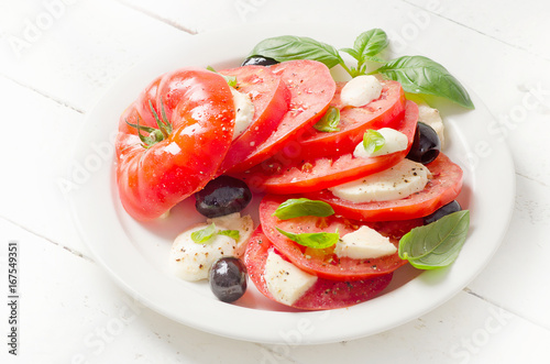 Tomato and mozzarella slices with basil leaves on a white plate.