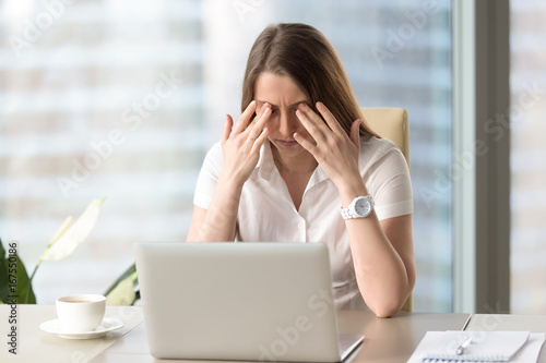 Young businesswoman doing exercises at workplace to relieve tired of computer eyes, massaging closed eyelids to relax muscles, reduce tension, improve vision, yoga for eye strain, eyesight relaxation photo