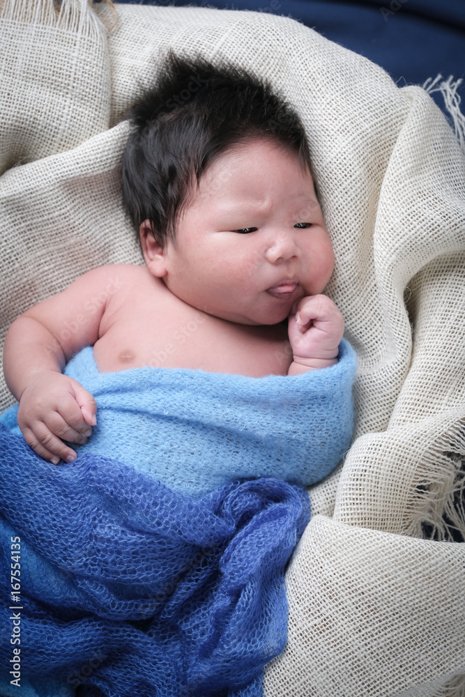 cute asian boy newborn portrait wrap blue fabric in basket on dark blue background fabric. cute asian boy newborn portrait wrap blue fabric in basket on dark blue background fabric.
