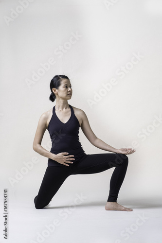 Portrait of mid Asian woman is playing yoga in studio in black sport wear.
