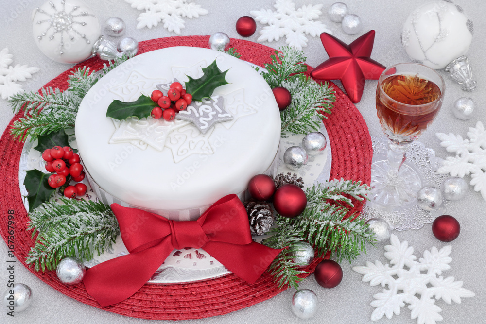 Iced Christmas cake with red bow, sherry drink, bauble and snowflake decorations, winter greenery and silver foil wrapped chocolates on glitter background. Iced Christmas cake with red bow, sherry drink, bauble and snowflake decorations, winter greenery and silver foil wrapped chocolates on glitter background.