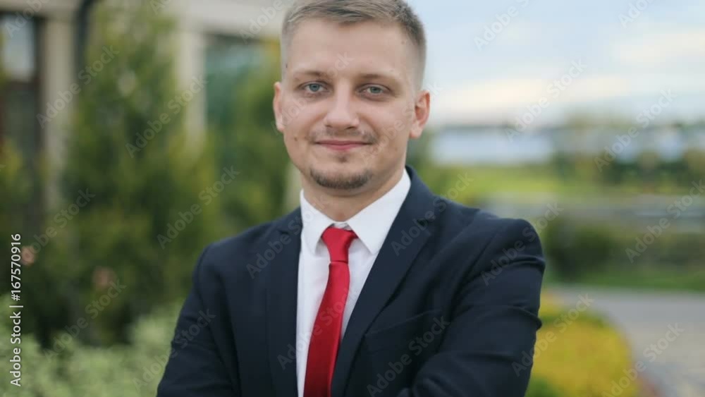 Portrait smiling handsome businessman arms folded over crossing hands crossed suit white shirt red tie outside blonde bearded beard attractive guy man young standing closeup shoulders looking camera Portrait smiling handsome businessman arms folded over crossing hands crossed suit white shirt red tie outside blonde bearded beard attractive guy man young standing closeup shoulders looking camera