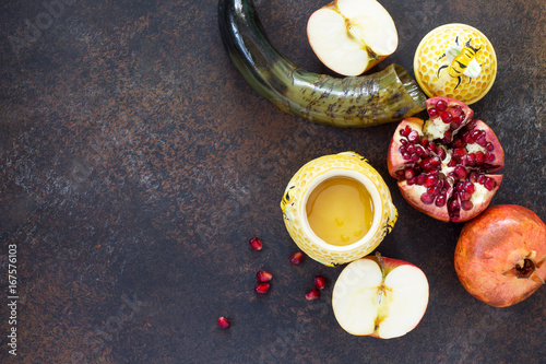 The concept of Rosh hashanah (Jewish New Year). Traditional holiday symbols - shofar, honey, apple and pomegranate on a stone or slate background. Flat lay, top view. photo