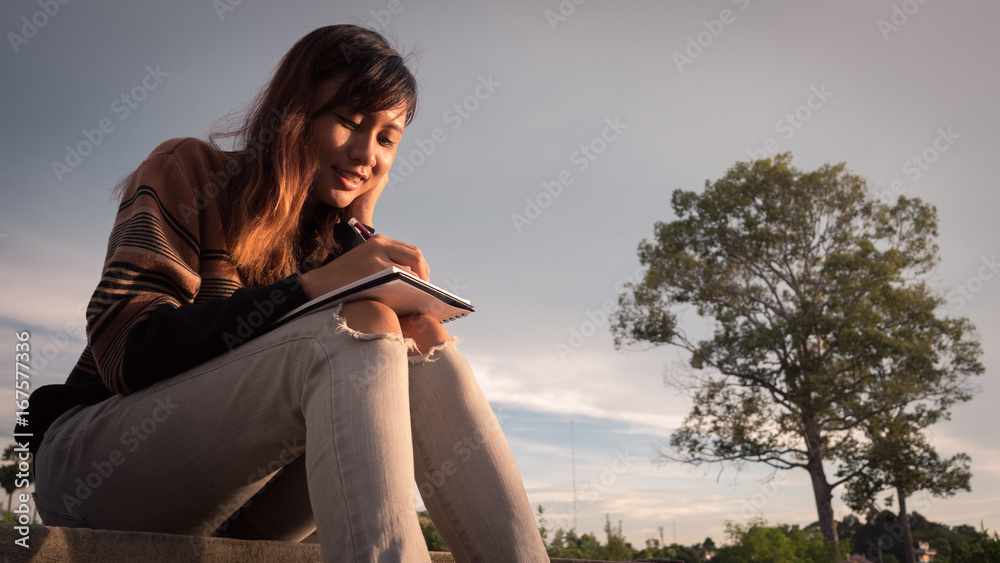 Young woman with pen writing on notebook at nature. Young woman with pen writing on notebook at nature.