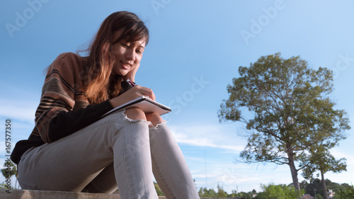 Young woman with pen writing on notebook at nature.