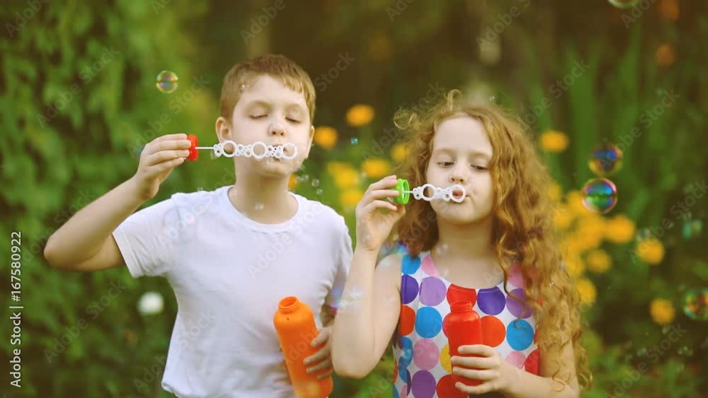 Happy boy and girl blowing soap bubbles in summer park. Slow motion. Happy boy and girl blowing soap bubbles in summer park. Slow motion.