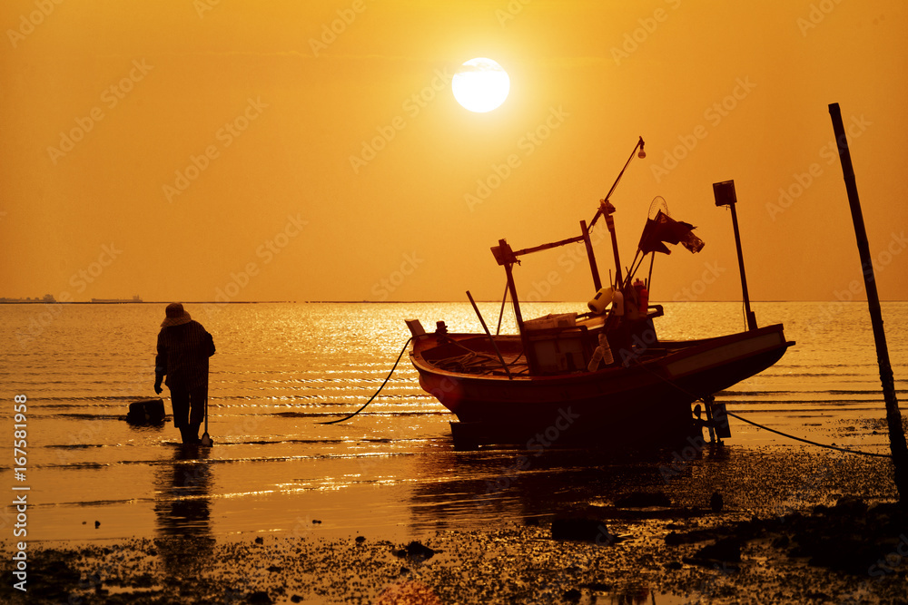 Silhouette of man and wooden fishing boat on sand beach