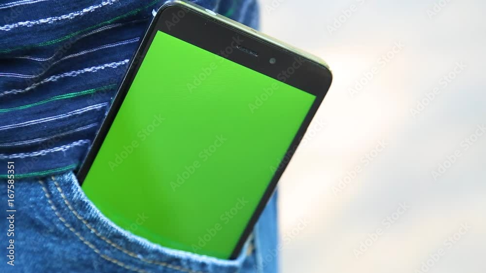 Closeup front view of modern black smartphone with blank green touch screen inside of pocket of blue denim jeans. Real time full hd video footage.