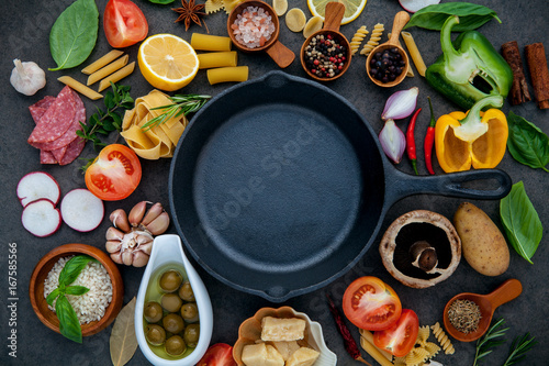 Italian food cooking ingredients on dark stone background with iron pan flat lay and copy space.