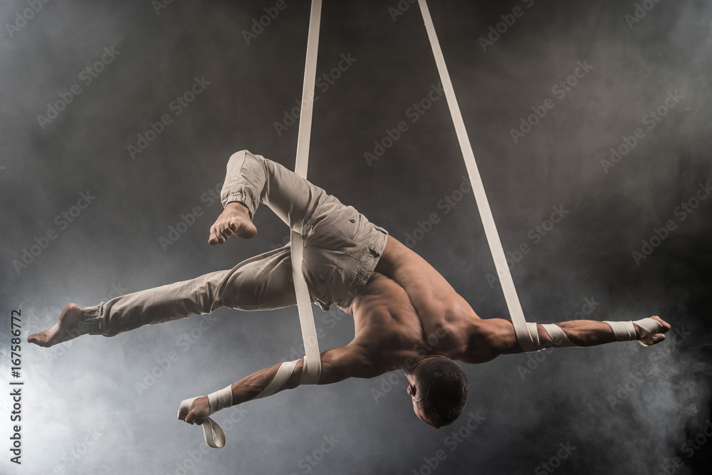 Foto Stock circus artist on the aerial straps with Strong muscles on the  background of smoke | Adobe Stock