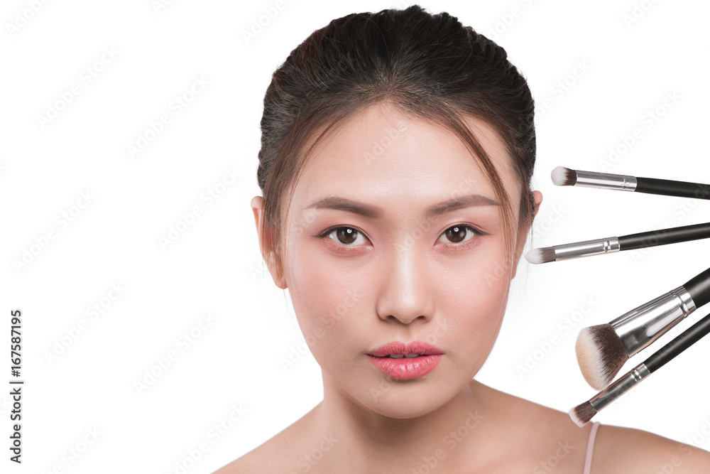 Fototapeta premium A portrait of young pretty isolated on white background women holding makeup brushes