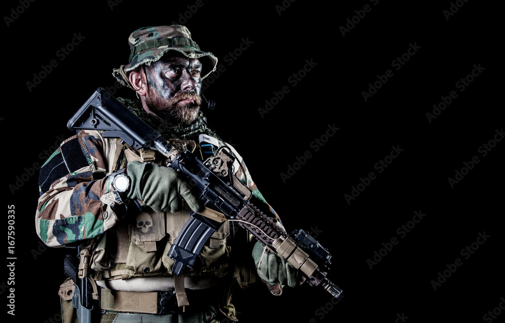 Bearded Special forces United States in Camouflage Uniforms studio shot half length black background. Holding weapons, wearing jungle hat, Shemagh scarf, he is ready to kill. Backlit