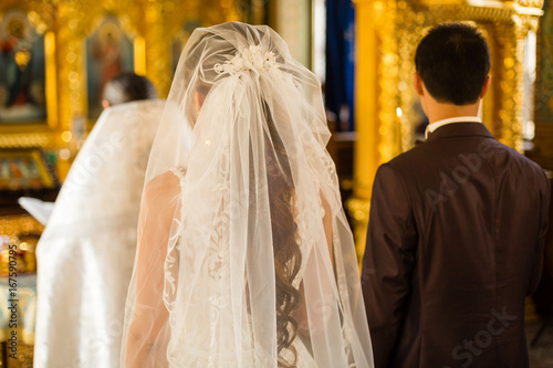 gorgeous bride and stylish groom holding candles at official wedding ceremony in old church. traditional moment