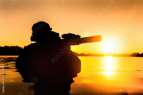 Silhouette of special forces with rifle in action during river raid in the jungle waist deep in the water. Proflie side view, half length photo