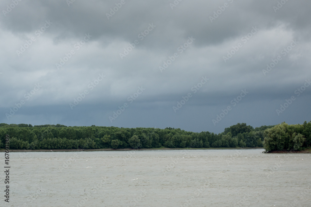 Thunderclouds over the Danube river in the spring. The strong wind and clouds pass on the river. Dark dramatic rain clouds over countryside landscape in Braila, Romania