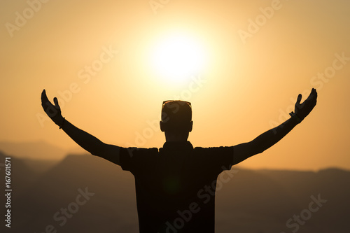 Young male against the light open arms at sunset