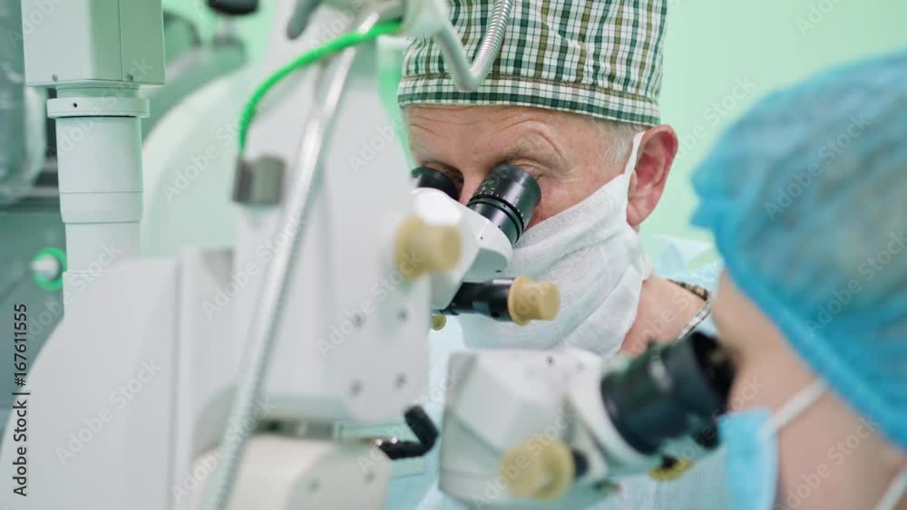 Team of ophtalmology surgeons and assistants with ophtalomological surgery tools during surgical treatment. Female and male surgeons operate the machinery. Indoor. Close up.