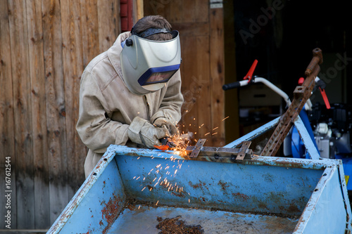 A young welder at work. The worker is engaged in welding parts of the car trailer