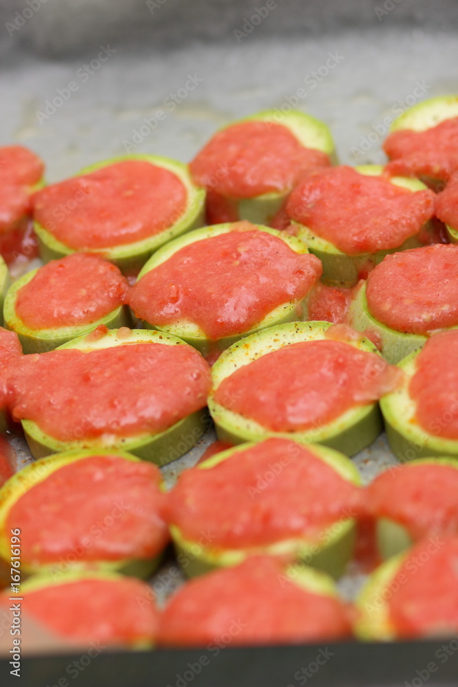 Sliced zucchini topped with tomato sauce before baking