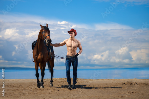 Macho man handsome cowboy and horse on the background of sky and water. © sheikoevgeniya