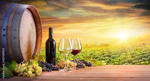 Wine Glasses And Bottle With Barrel In Vineyard At Sunset
