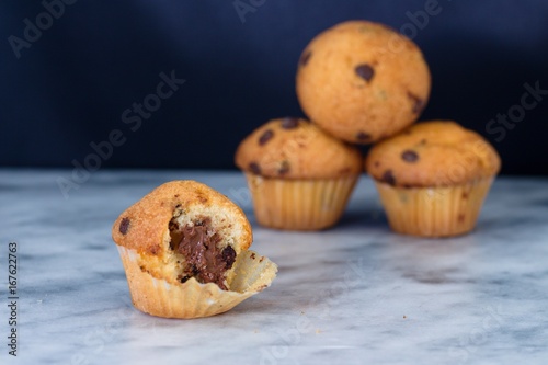 Half eaten vanilla muffin with cocoa filling and chocolate chips on marble surface