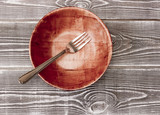 Empty wooden plate with a fork on a wooden table.