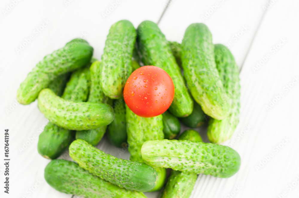 Single red tomato and heap of green fresh cucumbers on white rustic background Single red tomato and heap of green fresh cucumbers on white rustic background