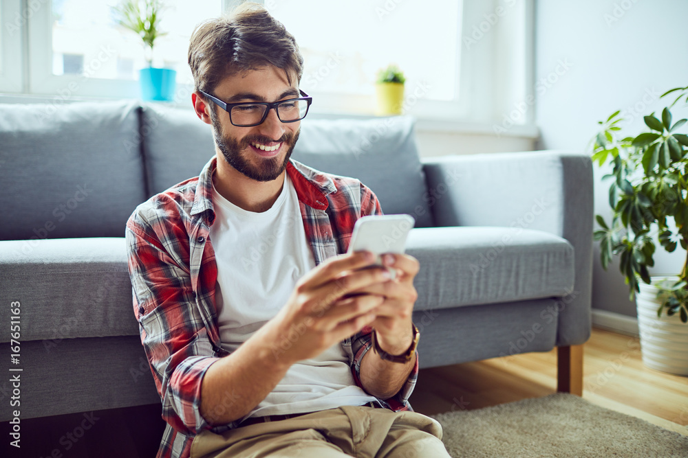 © baranq - Smiling young man sitting on floor and texting friend © baranq - Smiling young man sitting on floor and texting friend