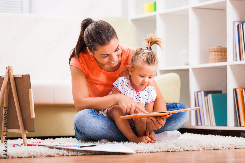 Mother and daughter in their home. They are looking at coloring book. Mother and daughter in their home. They are looking at coloring book.