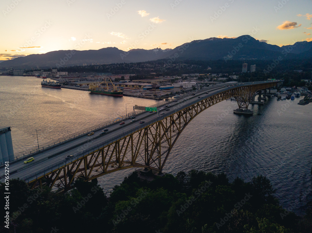 Obraz premium Aerial shot of bridge over river while sunset behind mountains