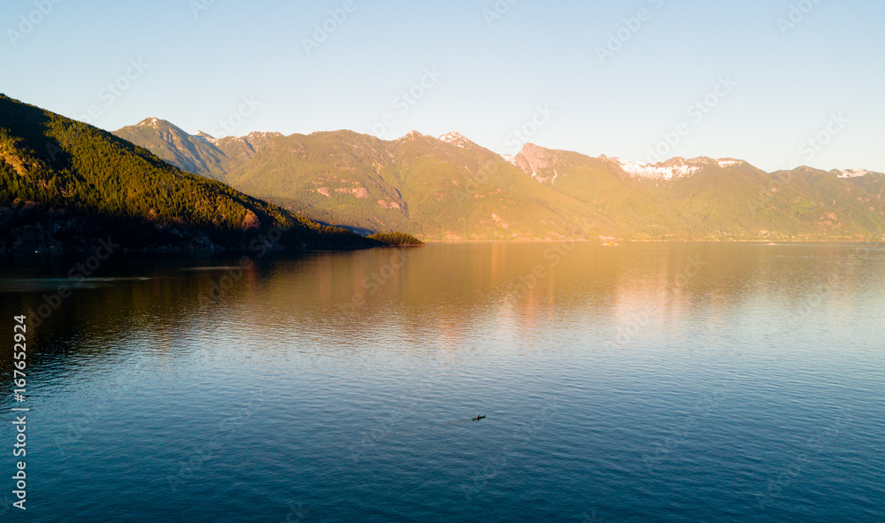 Aerial shot of kayaker on lake with mountains while  sunset