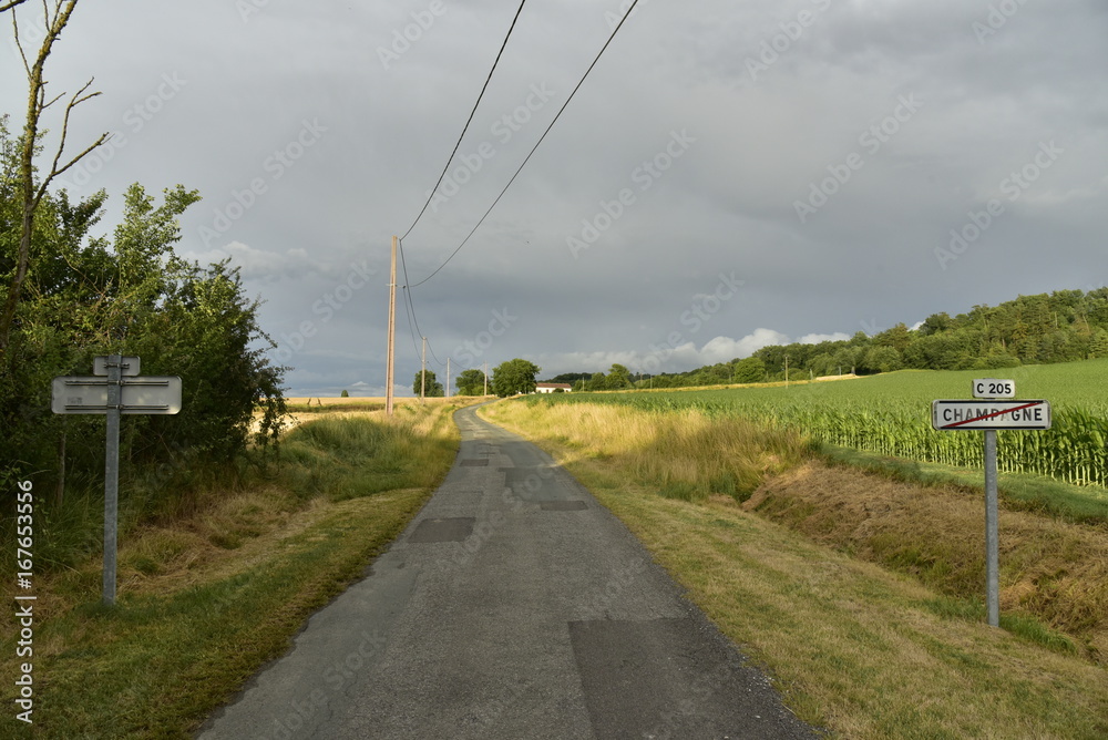 Petite route secondaire rurale sous la lumière du soir à la sortie du village de Champagne, au Périgord Vert